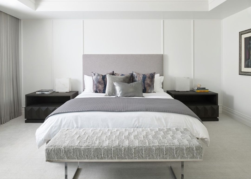 Harrison Fae Design - Upholstered furniture. This bedroom with white walls, a bedframe in grey with sheets in white and grey pillows, two black side tables, and covering all the room is a rug in grey.