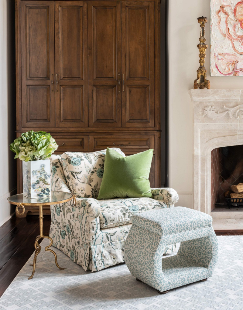 Dodson Interiors: Upholstered Furniture. This is a corner of a living room, near the fireplace we have Upholstered Furniture: a single sofa with a flower pattern, and a small ottoman in a blueish pattern.